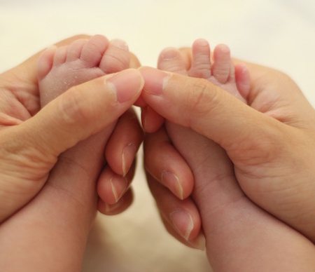 Shows an adult set of hands holding the feet of an infant
