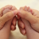 Shows an adult set of hands holding the feet of an infant