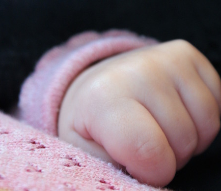 Shows a sleeping baby's hand on top of a pink baby blanket