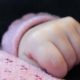 Shows a sleeping baby's hand on top of a pink baby blanket