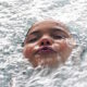 Shows a young child submerged in water with only his face showing