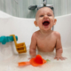 Shows a baby and it's toys on it's belly in a bathtub with a few inches of water