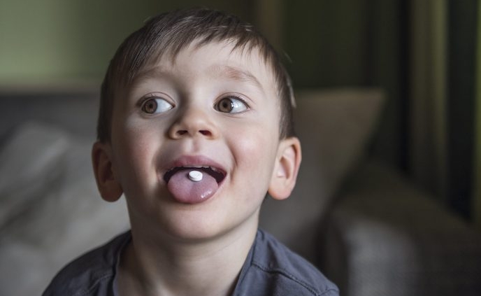 Shows a young boy sticking his tongue out and looking mischievous. His tongue has a pill on it.