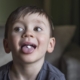 Shows a young boy sticking his tongue out and looking mischievous. His tongue has a pill on it.