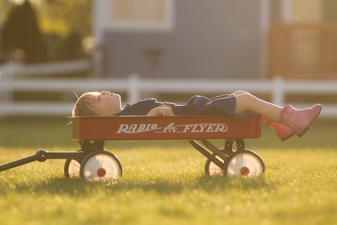 Shows a young girl on her back sleeping in a red Radio Flyer wagon