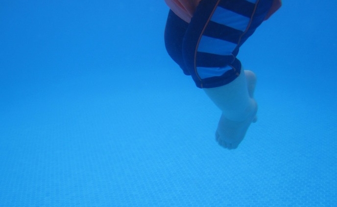 Shows the bottom portion of a toddler's body floating in the water. The child is wearing a life jacket.
