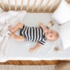 Image shows a baby on its back in a crib surrounded by blanket, pillows, and toys