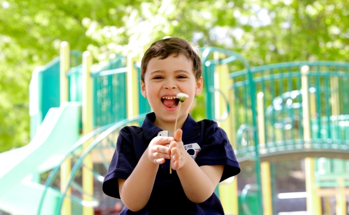 Shows a young boy on a playground. He is wearing a black shirt and holding a dandelion.