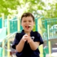 Shows a young boy on a playground. He is wearing a black shirt and holding a dandelion.