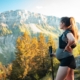 Shows a pregnant woman holding a walking stick as she stands on the peak of a mountain
